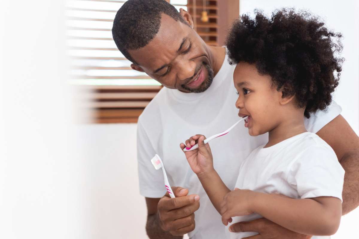 Dad helping kid brush teeth