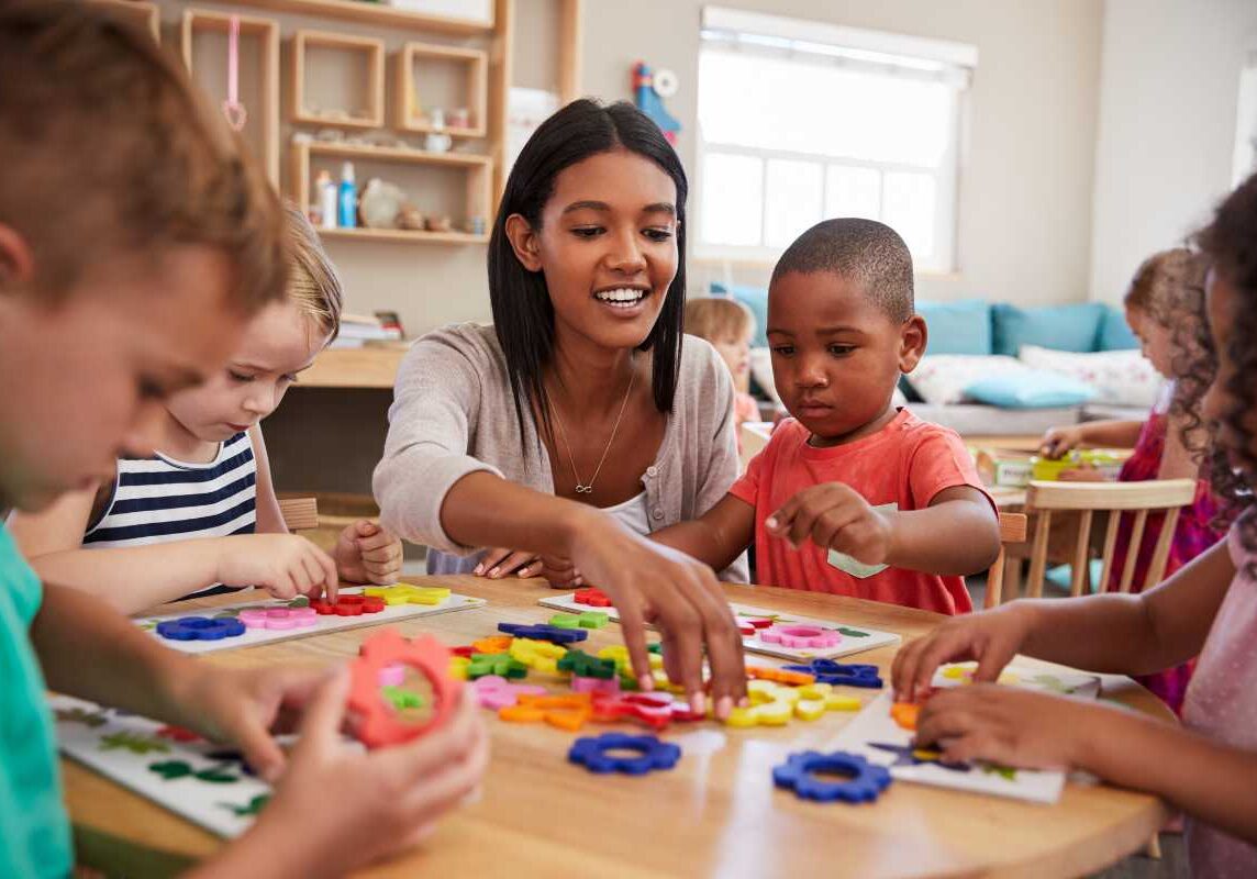 Child care teacher ensuring a strong start for children Child care teacher working with young students at a table